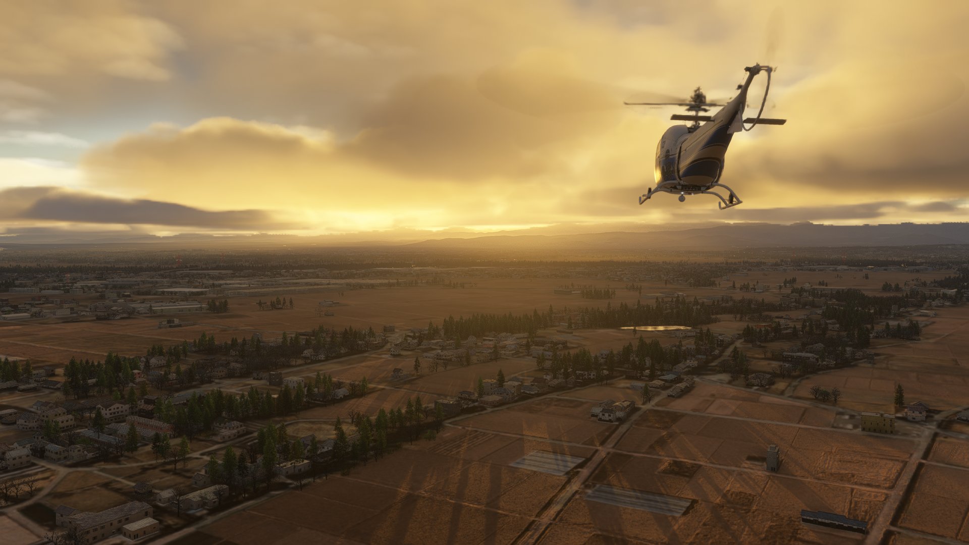 A helicopter in blue and white paint scheme flies towards a sunset