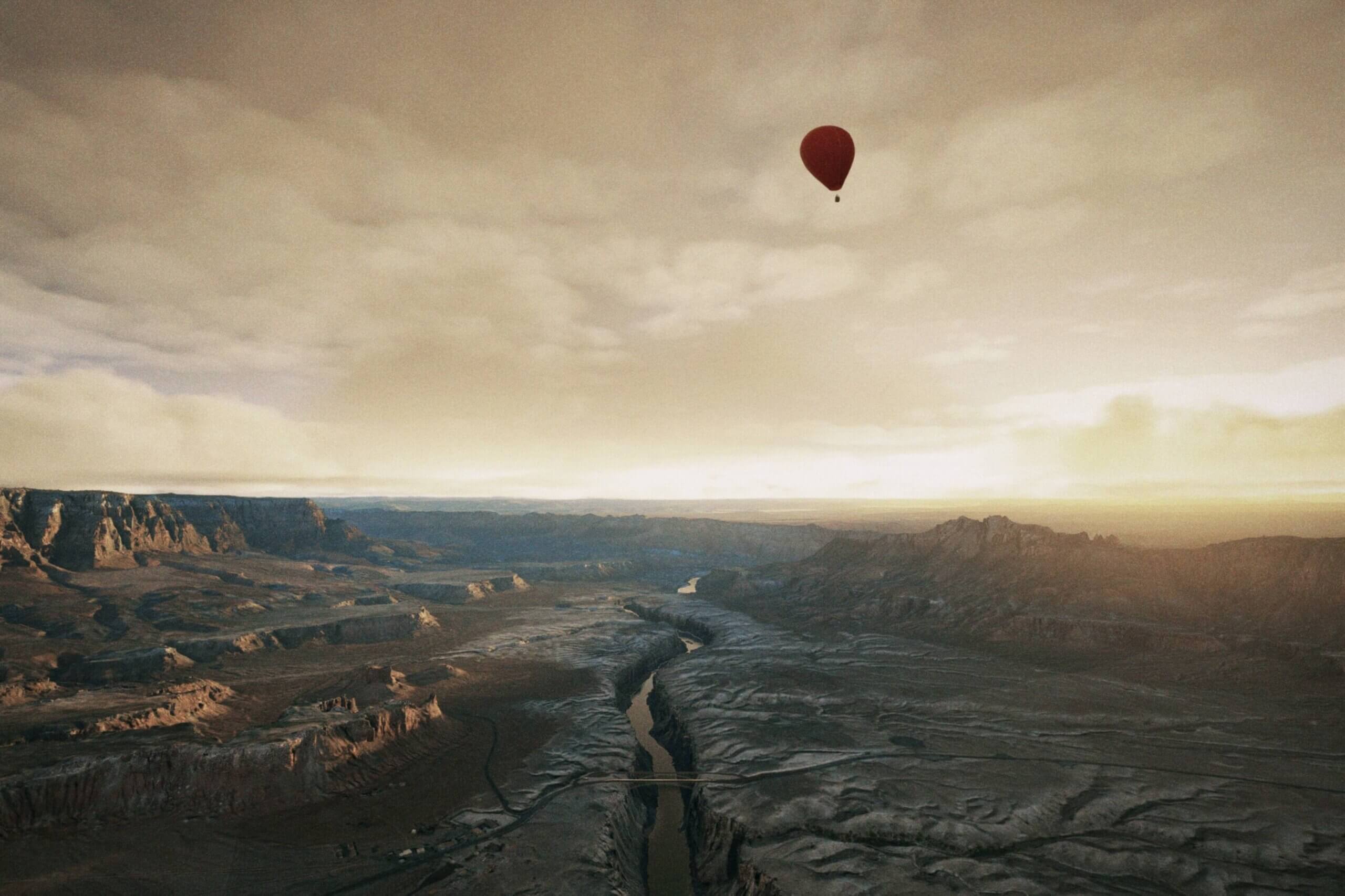 A Hot Air Balloon flies over a mountain range with overcast clouds above