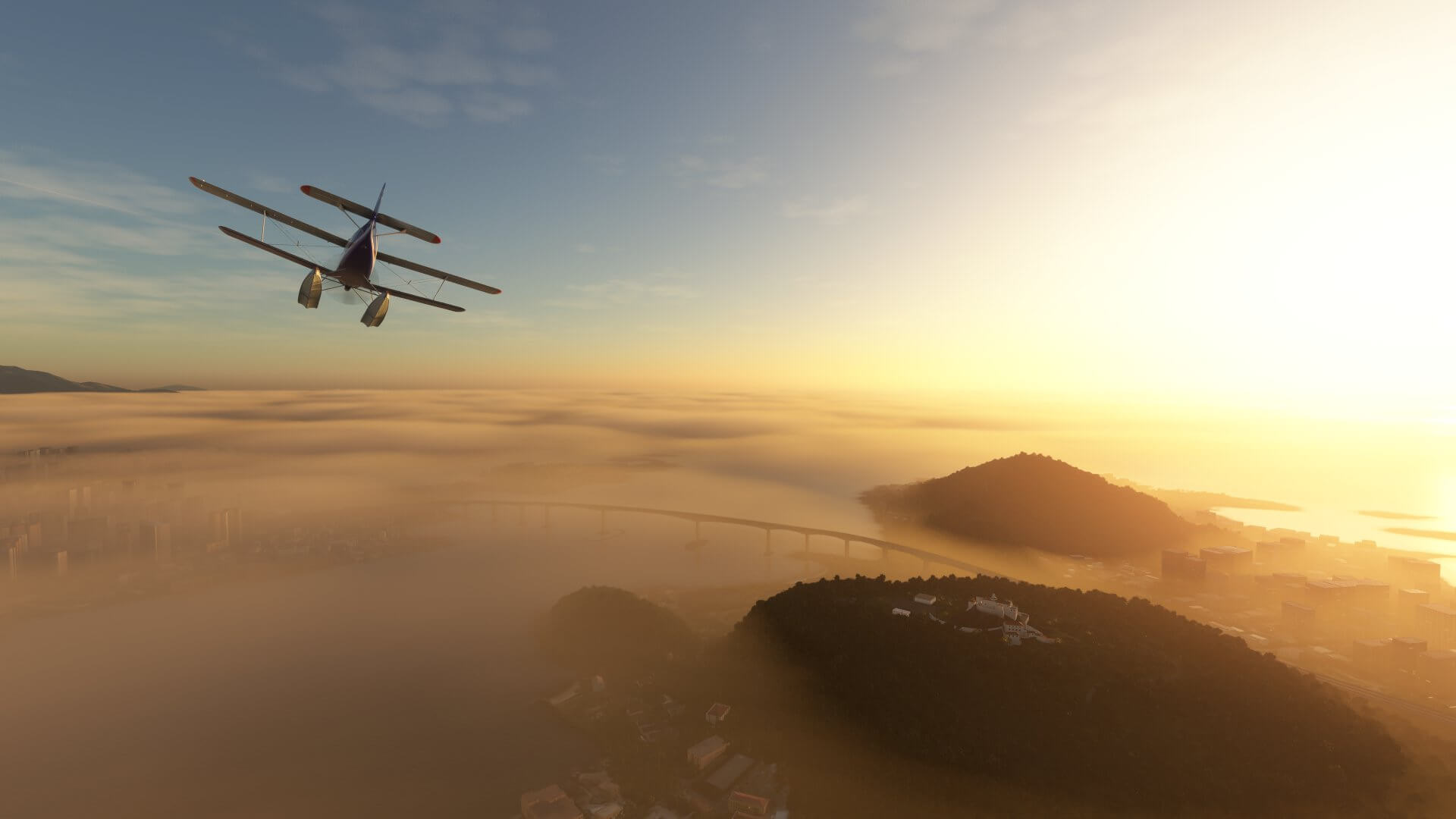 A dual wing float plane propeller aircraft flies over a city with a low cloud base during sunset