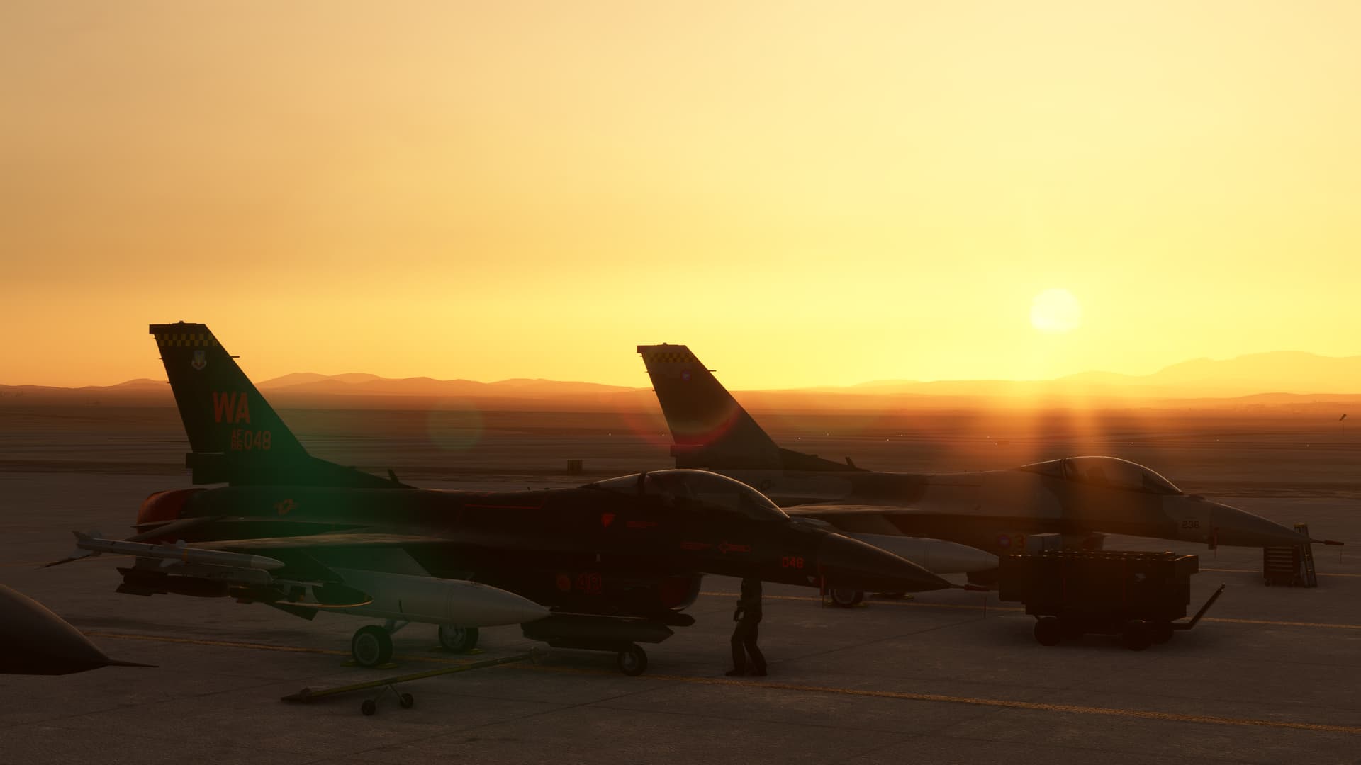 Two F-16's parked on the ramp with the sun setting in the distance