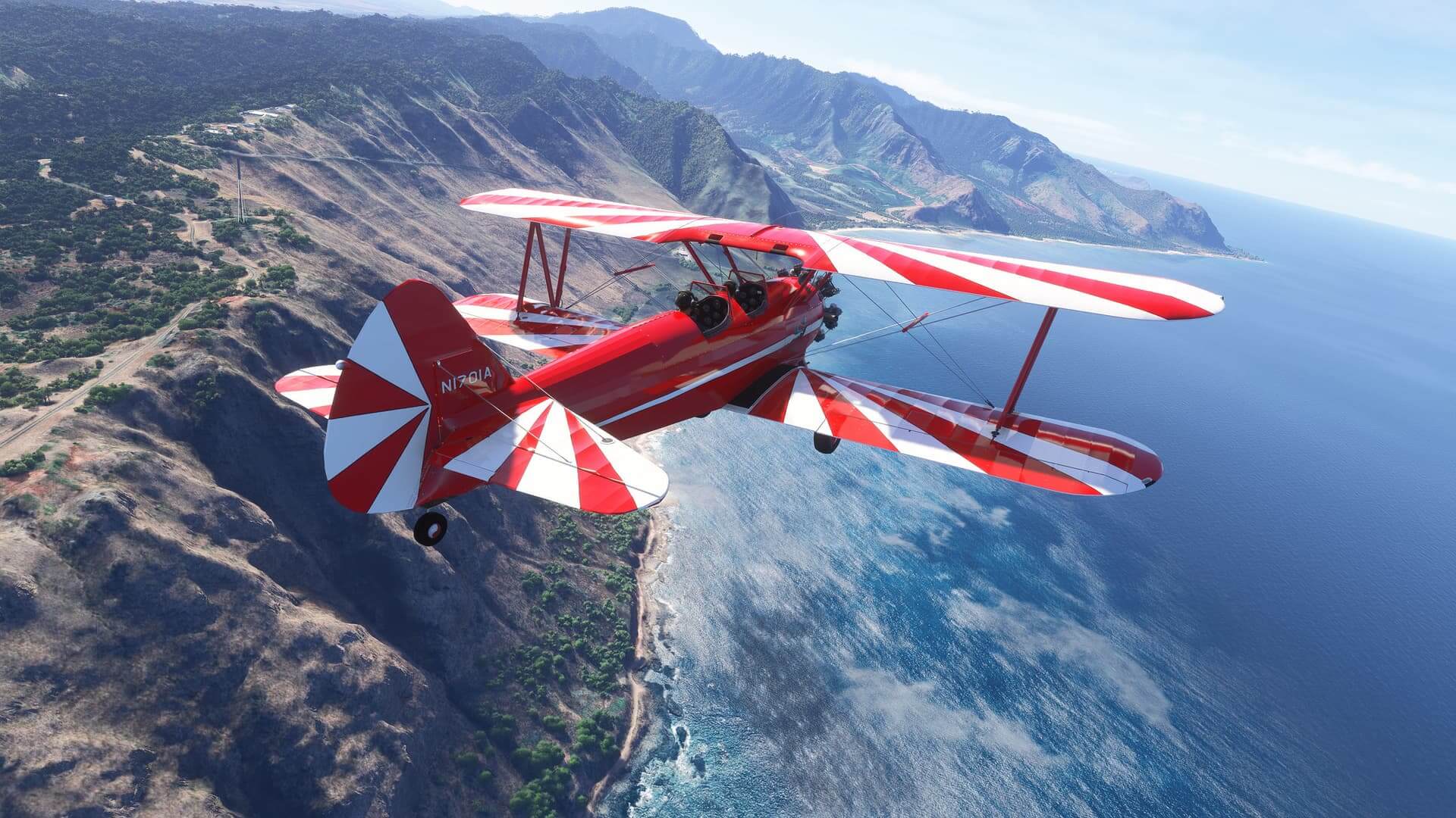 A dual wing propeller aircraft painted in red and white color scheme flies along a rocky mountain coastline