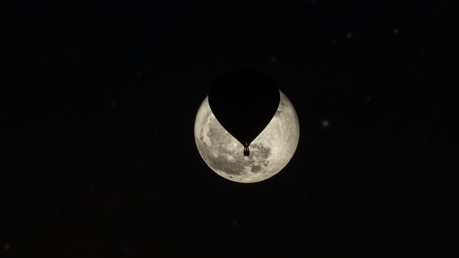 A hot air balloon is silhouetted by the moon behind