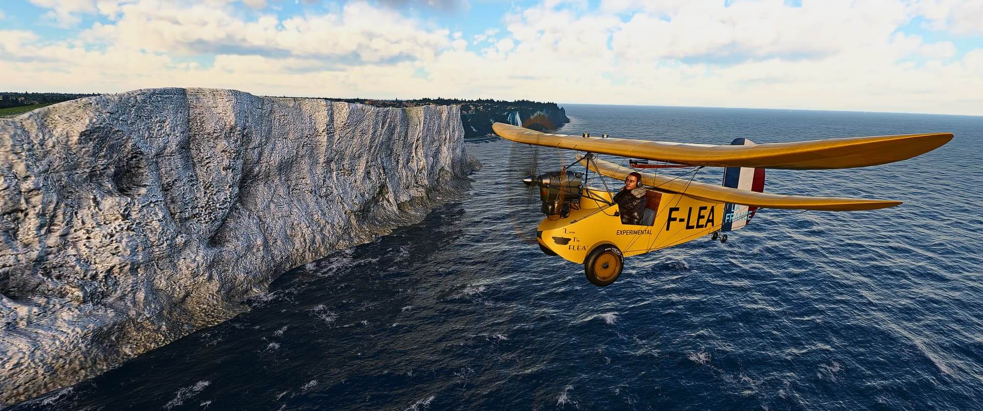 A dual wing orange propeller aircraft flies close to a tall cliff