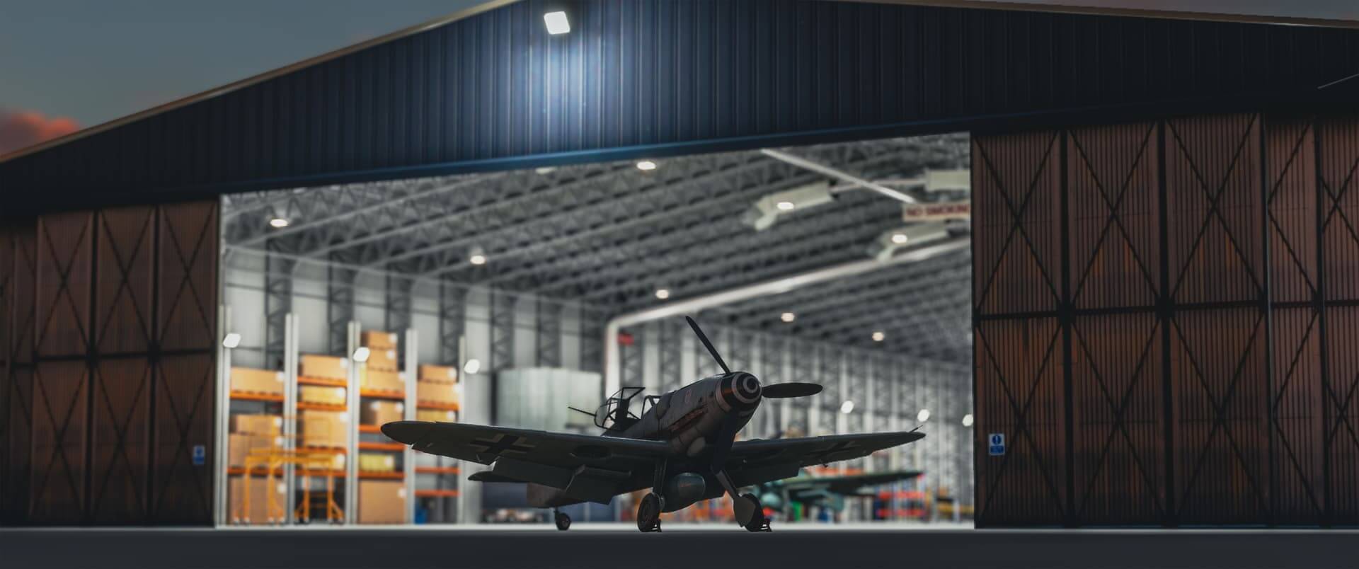 A warbird sits with canopy open in front of an open hangar