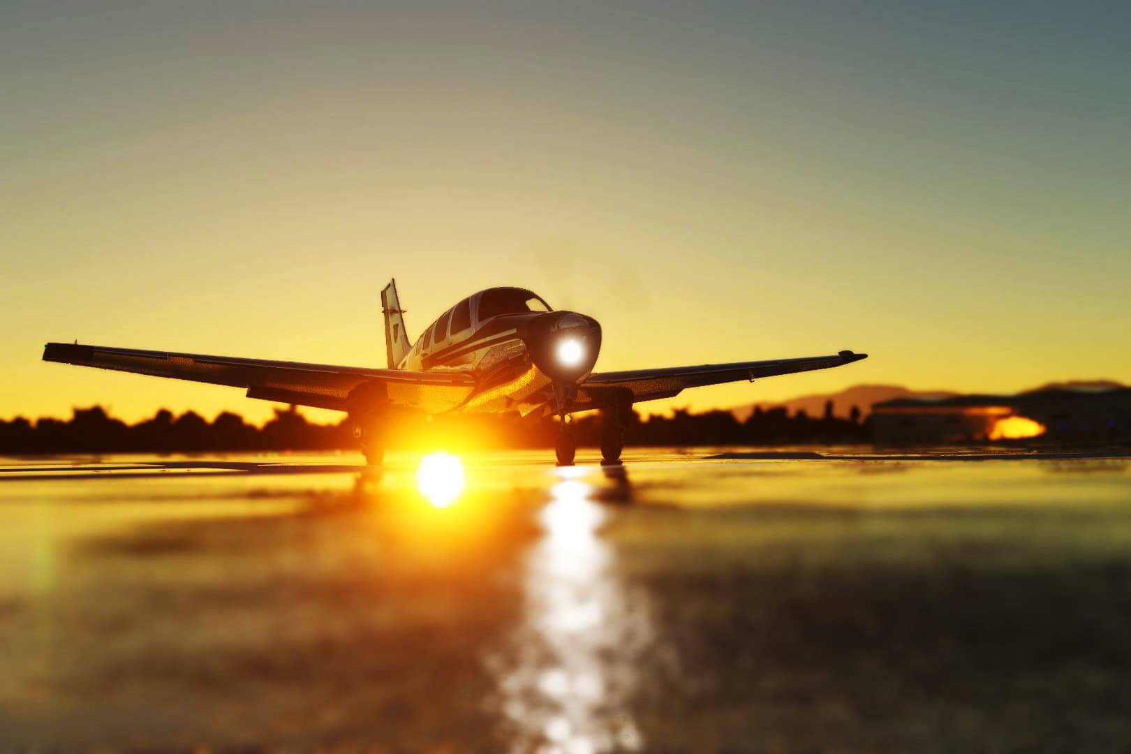 An aircraft sits on a damp runway and the setting sun reflects brightly off of the puddles.