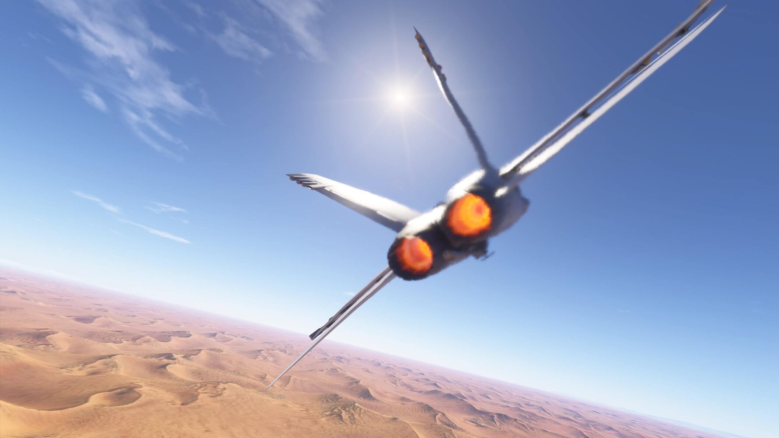 A jets afterburners are brightly lit as it flies above a desert on a bright sunny day.