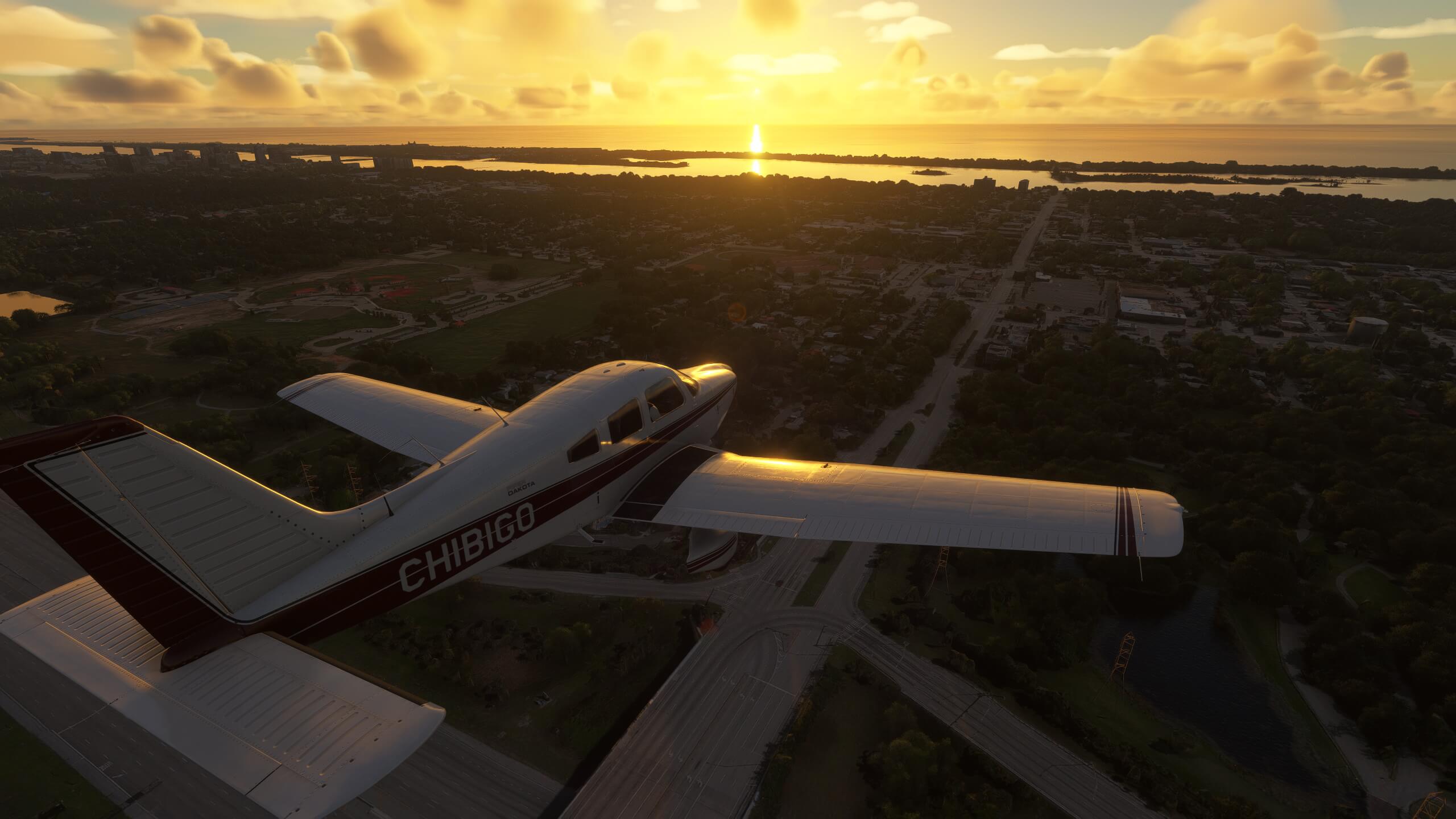 A Piper PA-28-236 Dakota flies towards a coastline with the sun setting in the distance