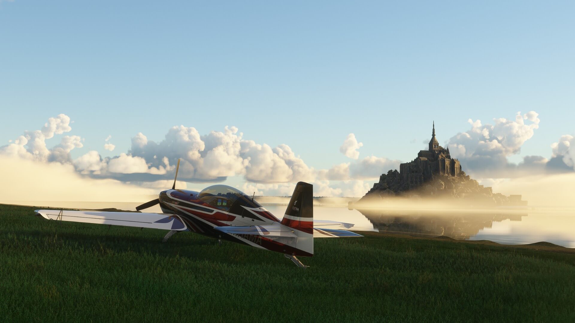 An Extra 330LT is parked on the grass in front of Mont St. Michel.