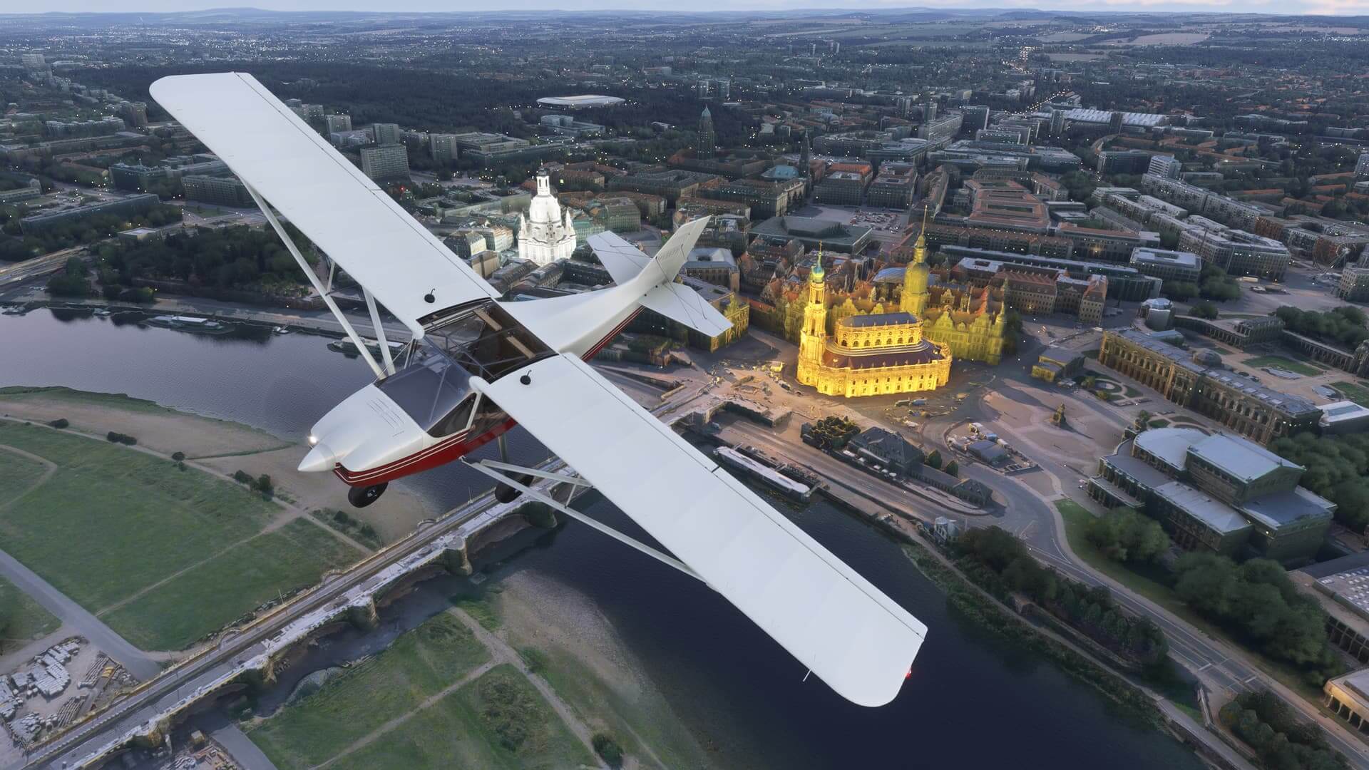 A high wing propeller aircraft flies over a busy city with cathedrals lit up below
