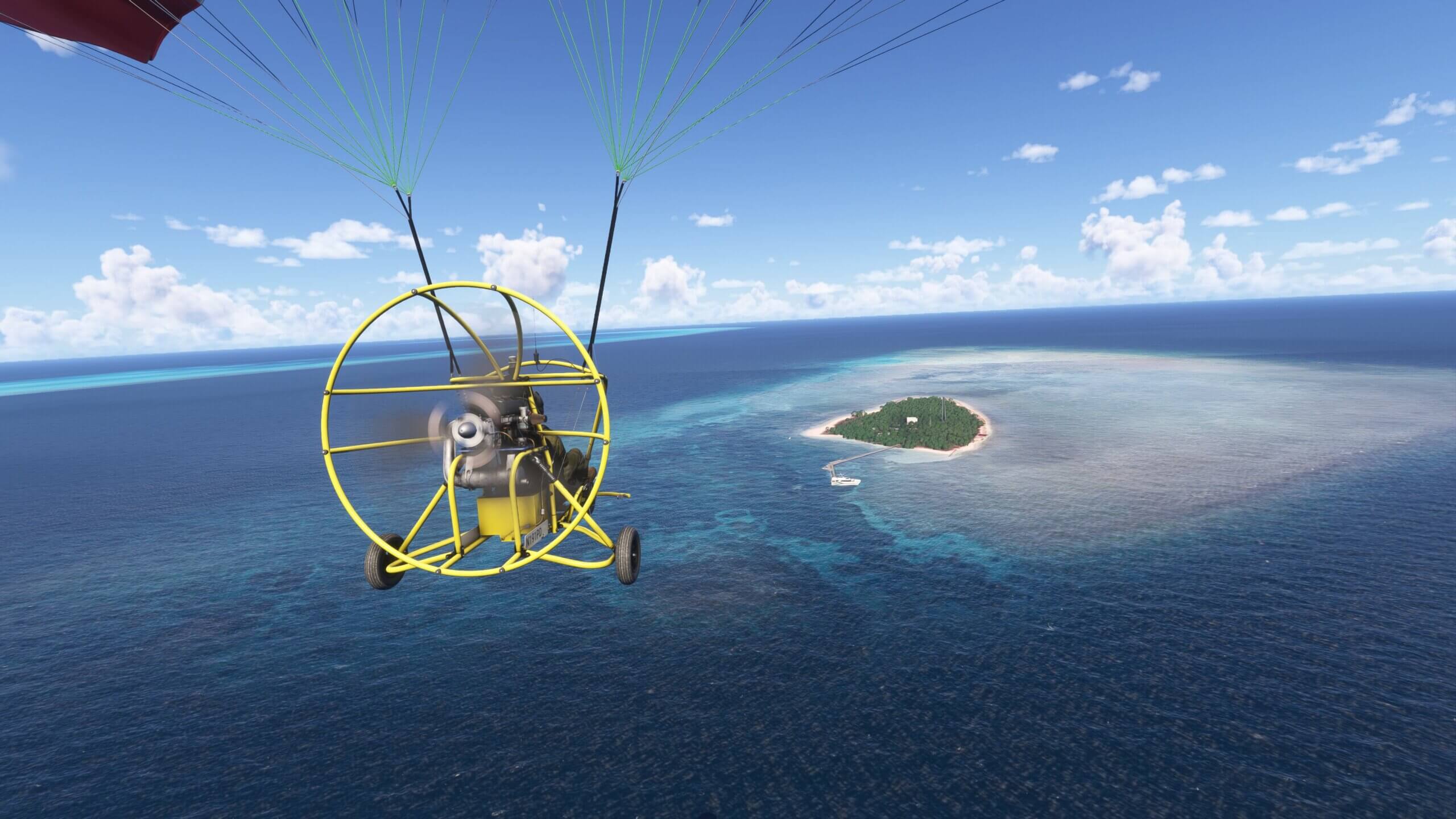 A gyrocopter flies towards an island populated with dense trees, with a yacht stationary near a jetty