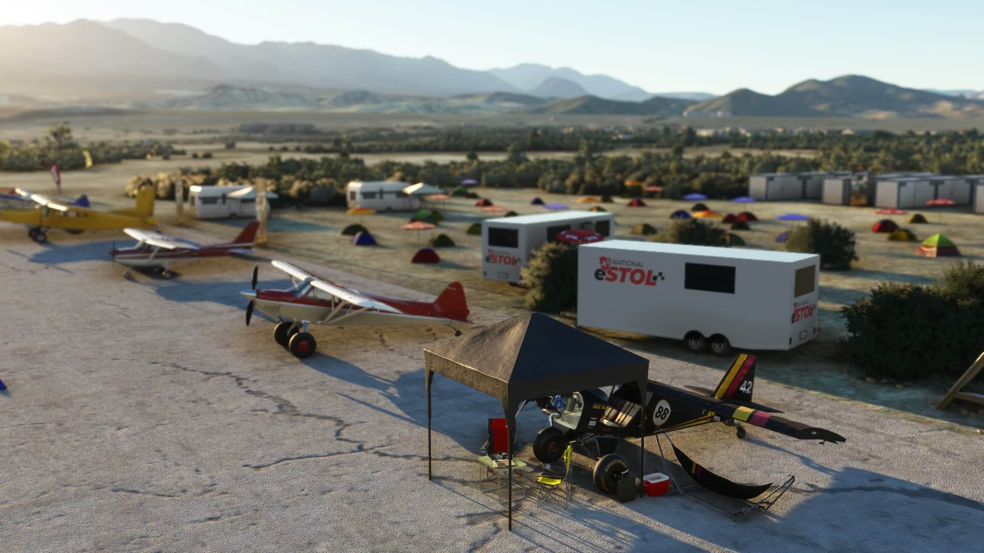 Numerous eStol aircraft are lined up on an apron, with a campsite in view behind