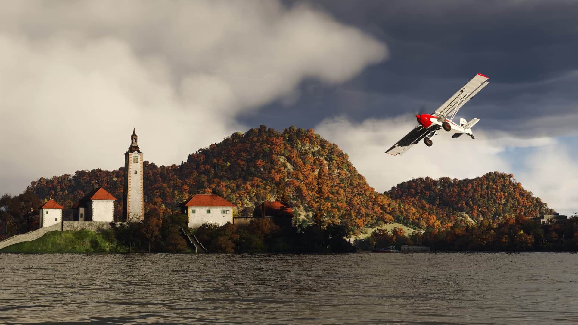 A high-wing propeller aircraft banks sharply to the right over water near an autumnal area of foliage