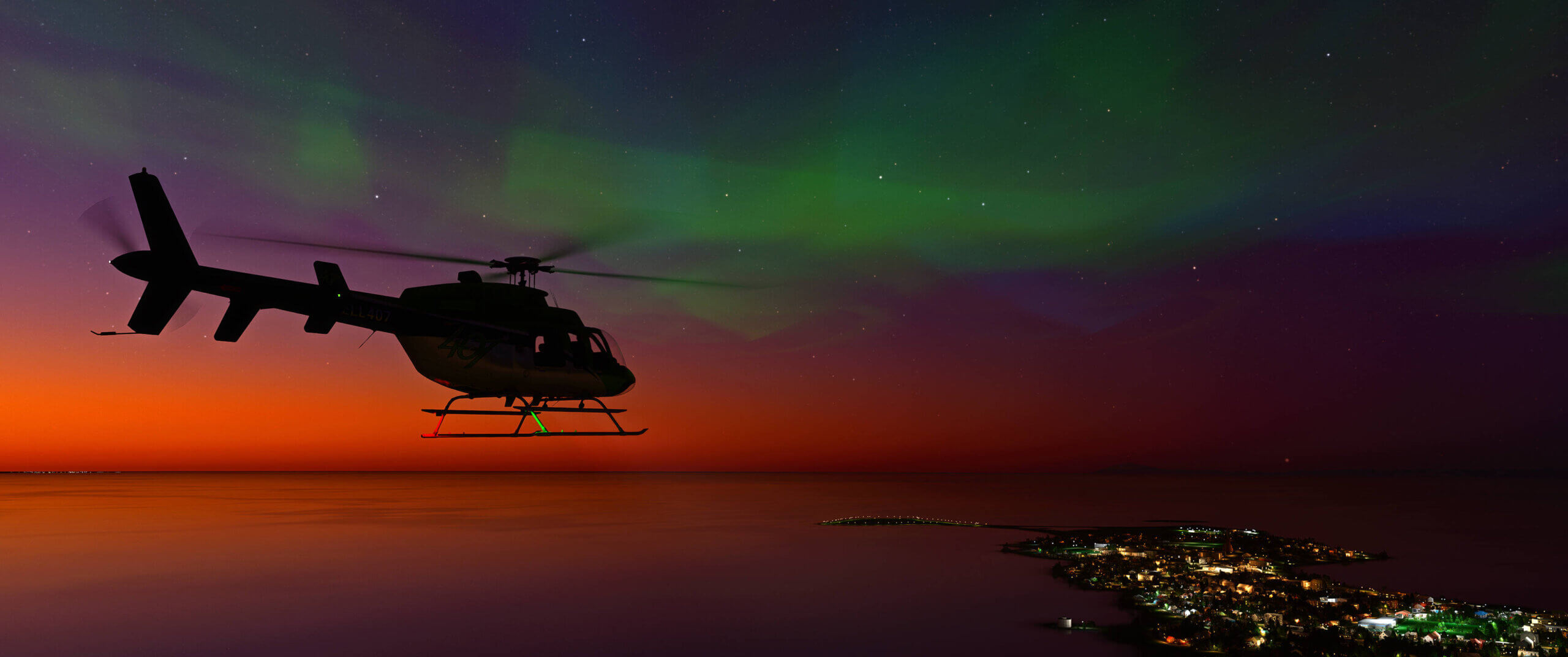 A Bell 407 helicopter cruises at night with the Aurora Borealis seen overhead