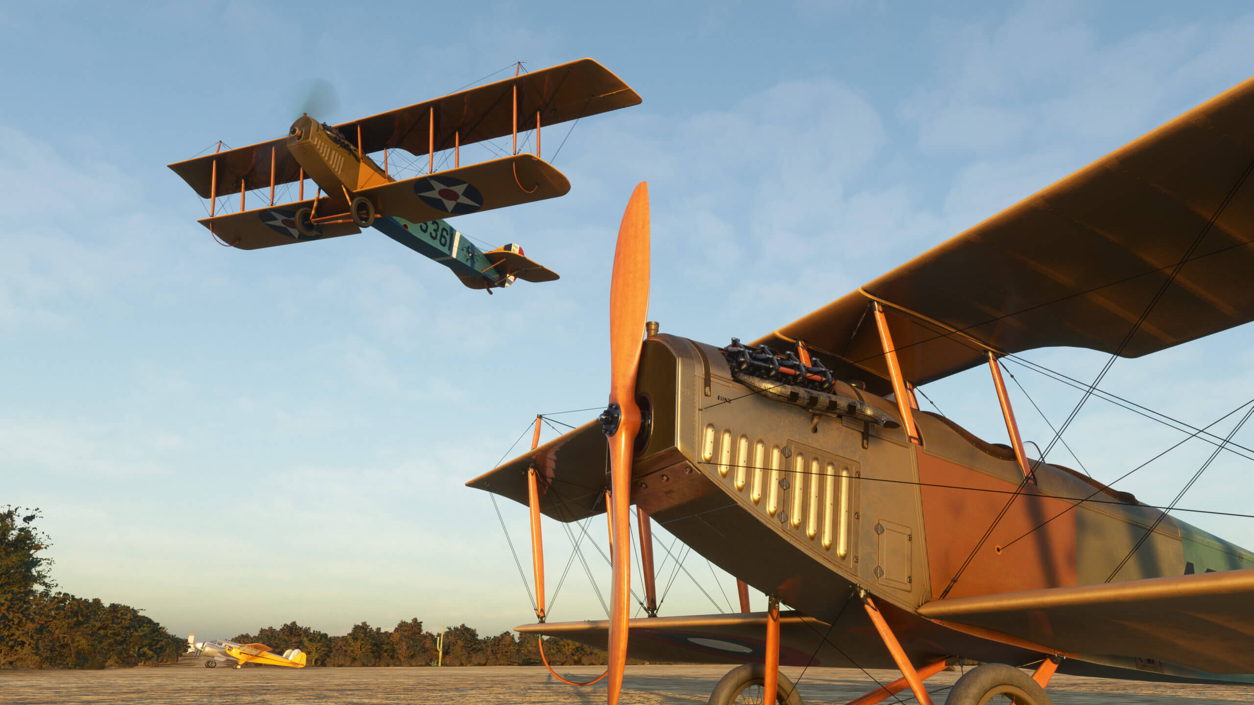 two dual wing vintage military aircraft are in view, with one parked on the ramp and the other flying directly above