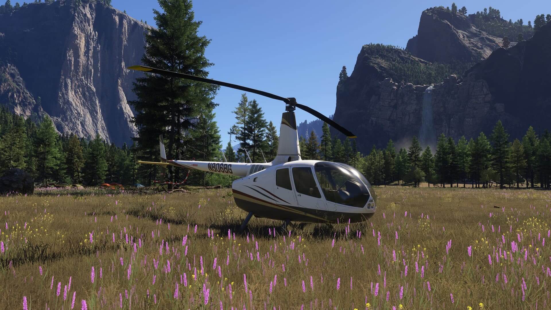 A Robinson R66 helicopter sits in a grass field between rocky terrain and a waterfall in the background