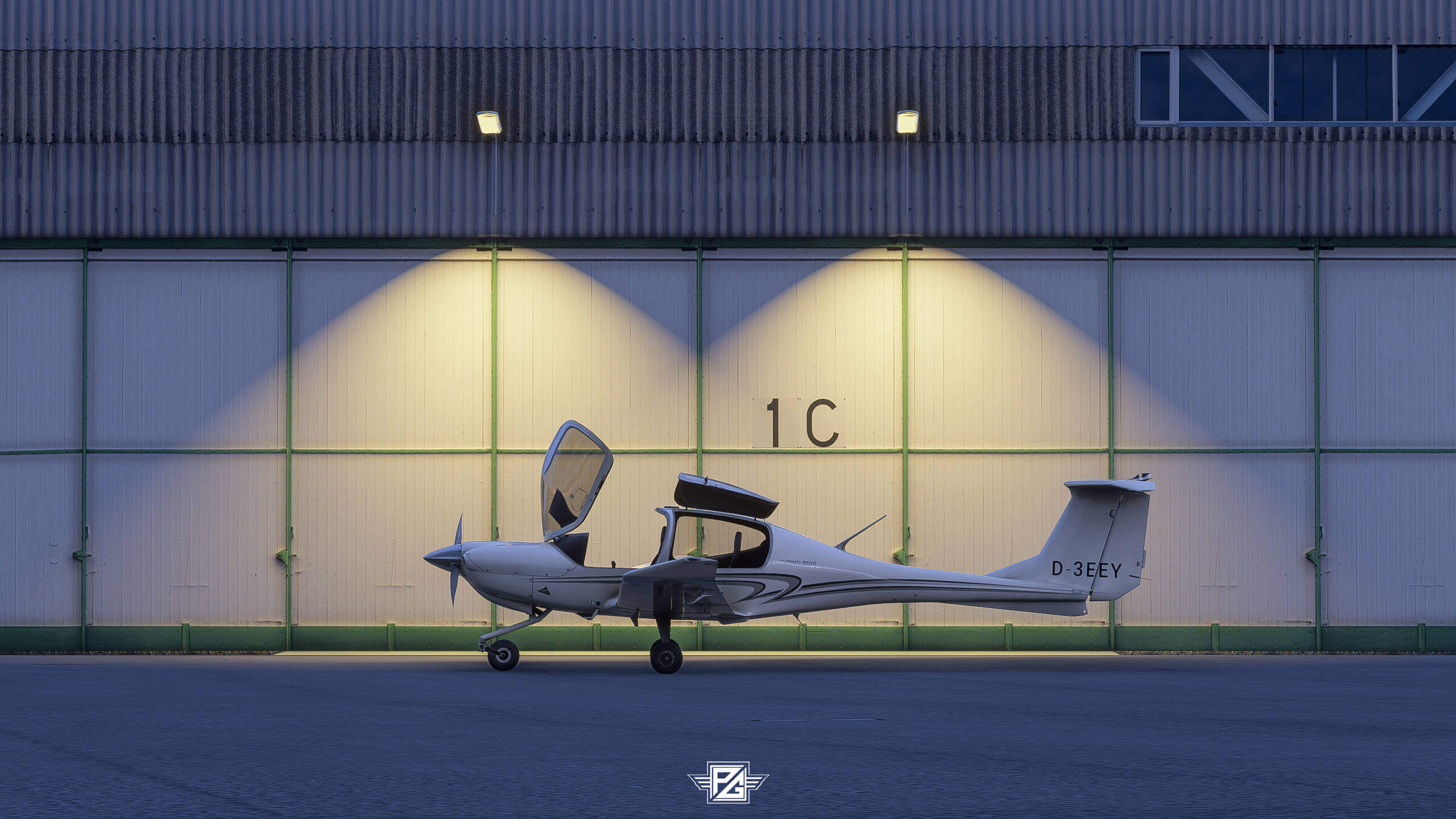 A low wing propeller aircraft has its canopy open whilst sitting idle on the ramp in front of an airport hangar