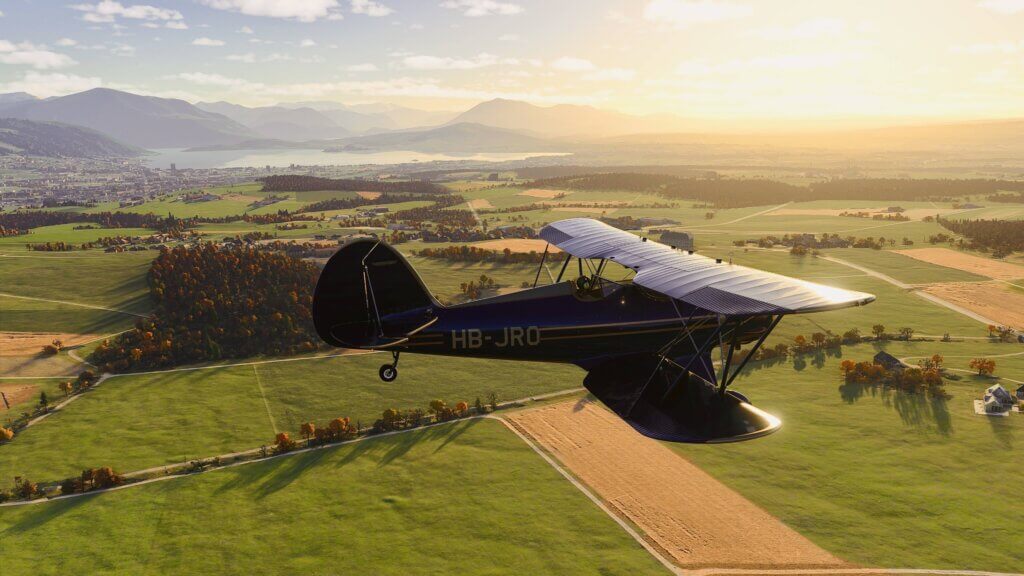 A dual wing propeller aircraft cruises low over fields with the sun reflecting off of its wings