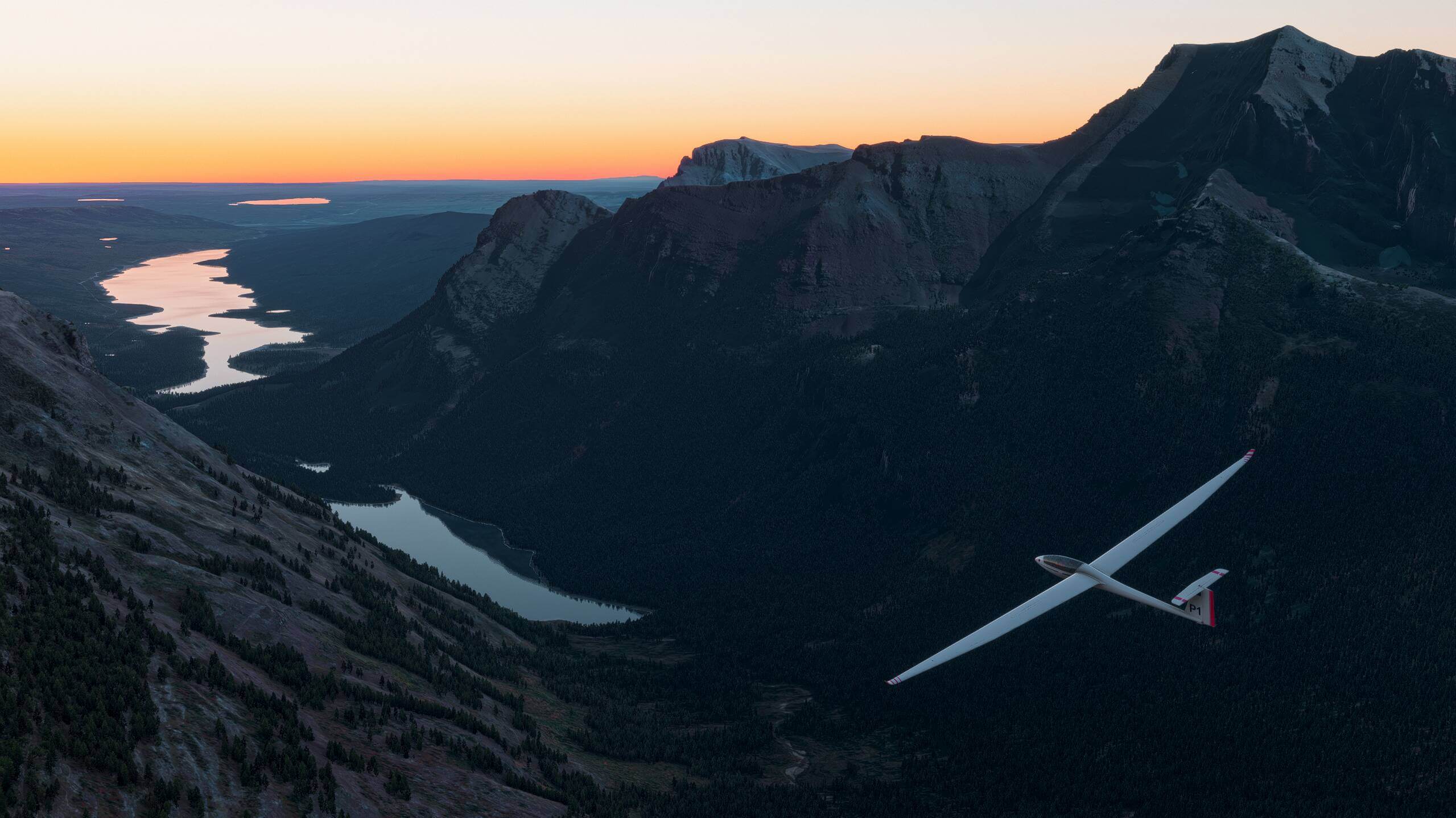 A glider flies through a valley after the sun has set in the distance