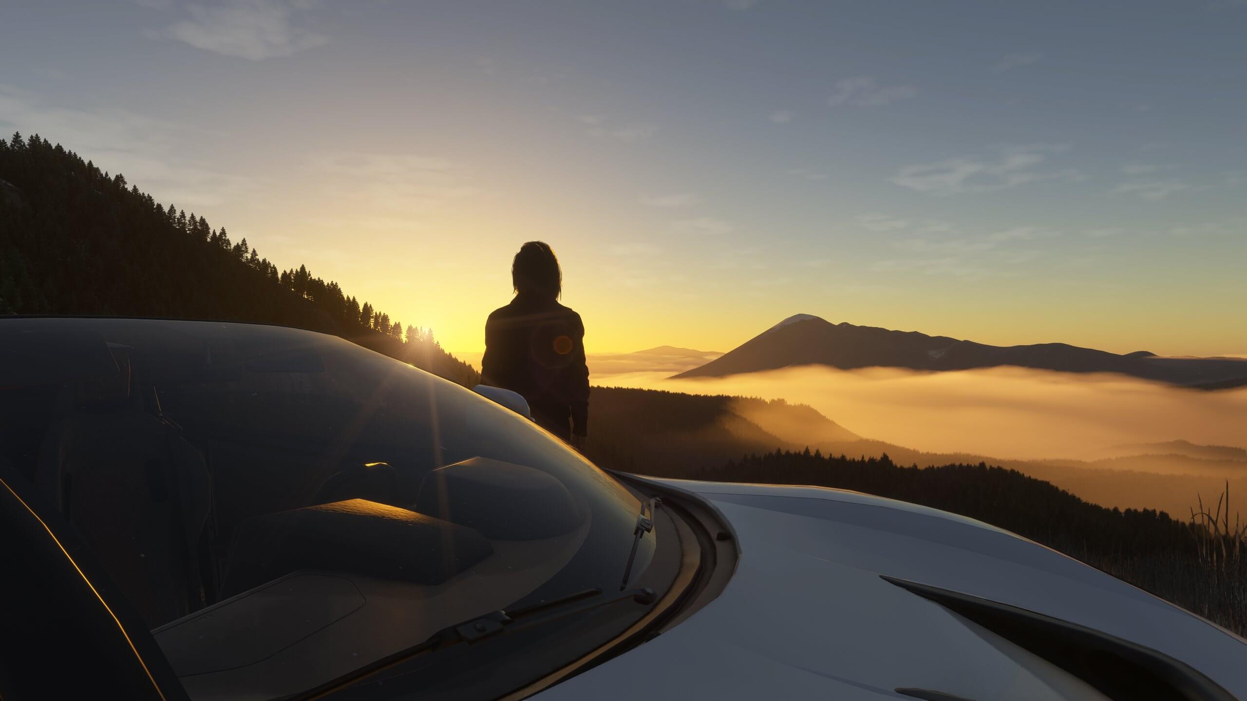 A person looking over a valley during sunset next to their car