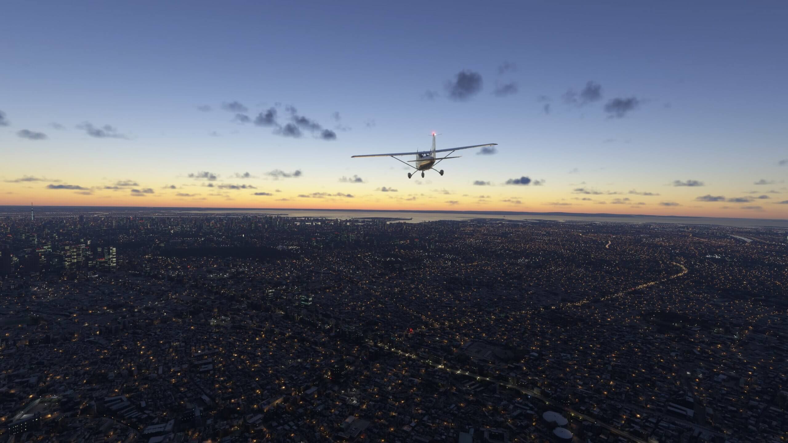 A Cessna 172 cruises above a city with street lamps still on before sunrise
