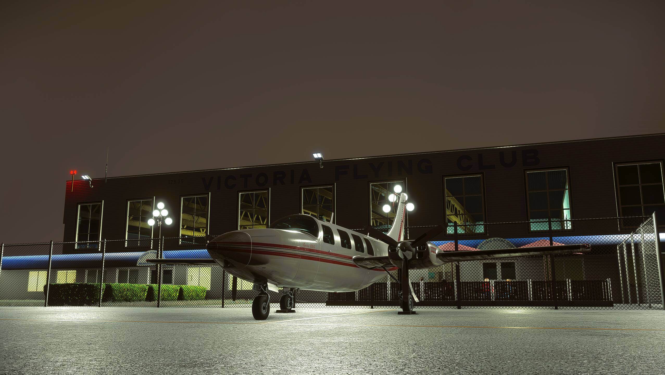 A dual propeller aircraft sits on the Victoria Flying Club ramp at night