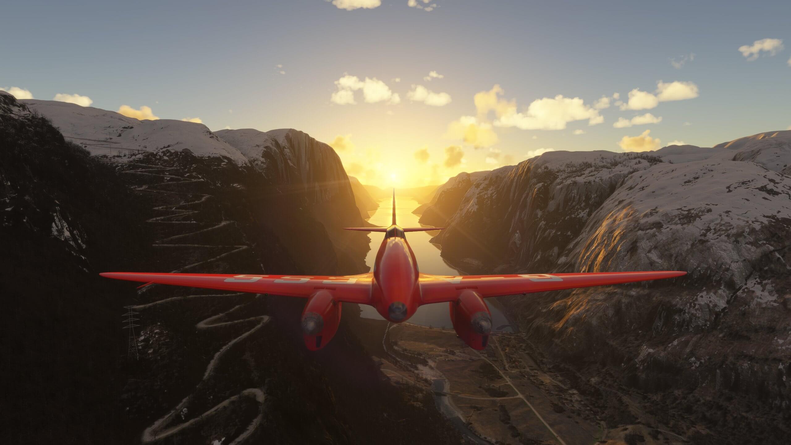 A red propeller aircraft flies down a valley with the sun setting directly behind