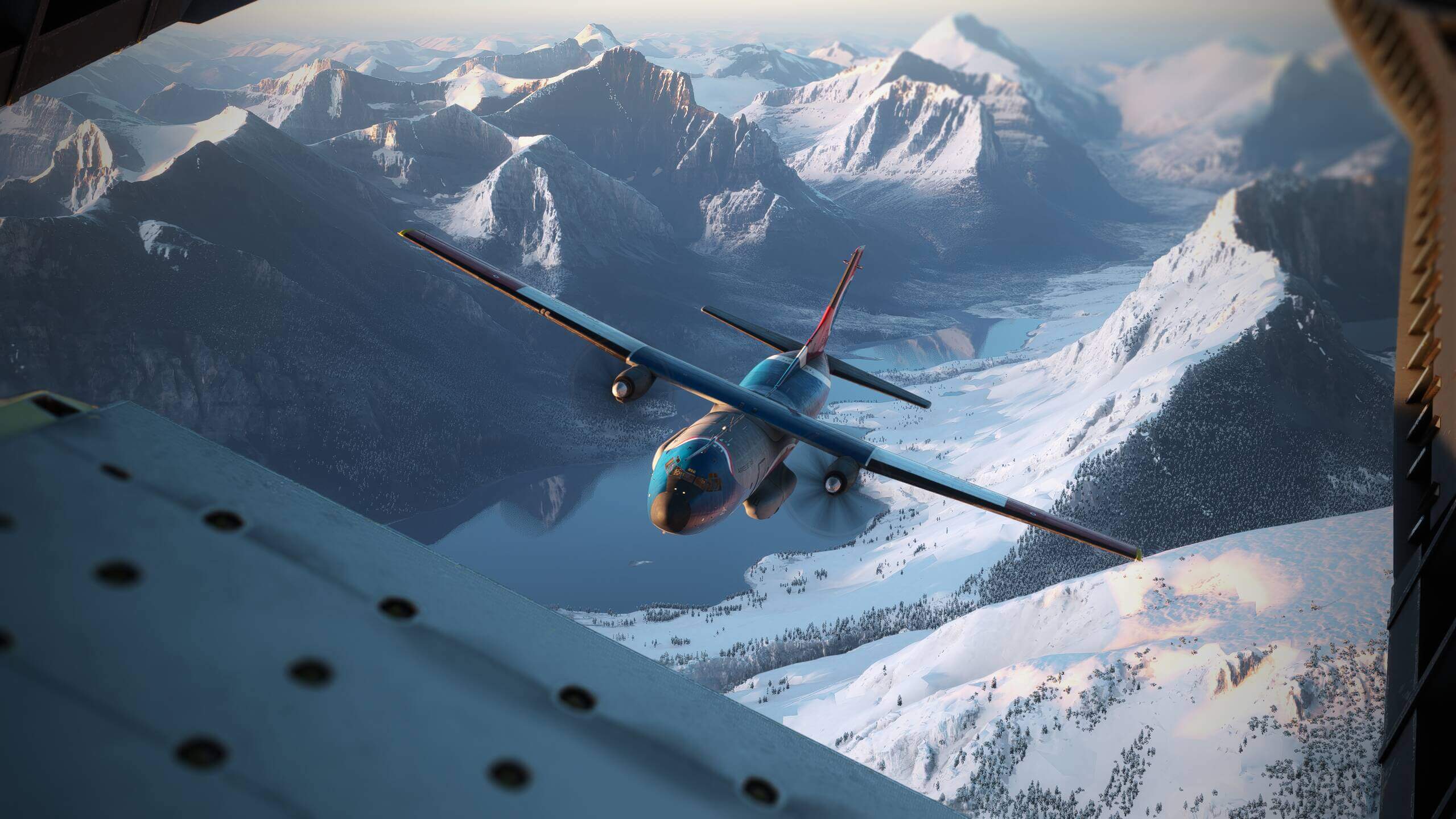 A high wing military aircraft flies through a snowy mountain range