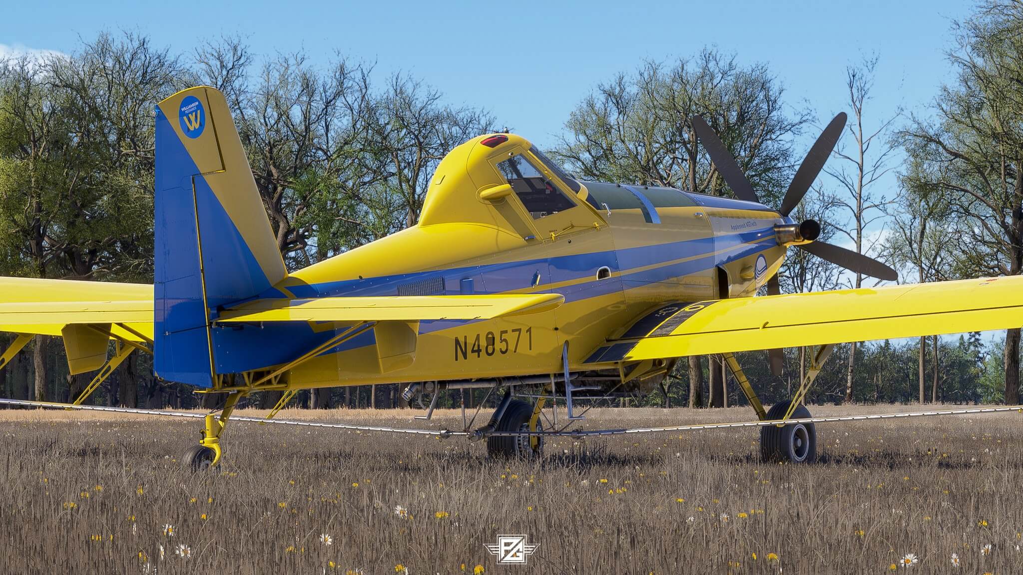 A crop dusting aircraft sits idle on a grass field