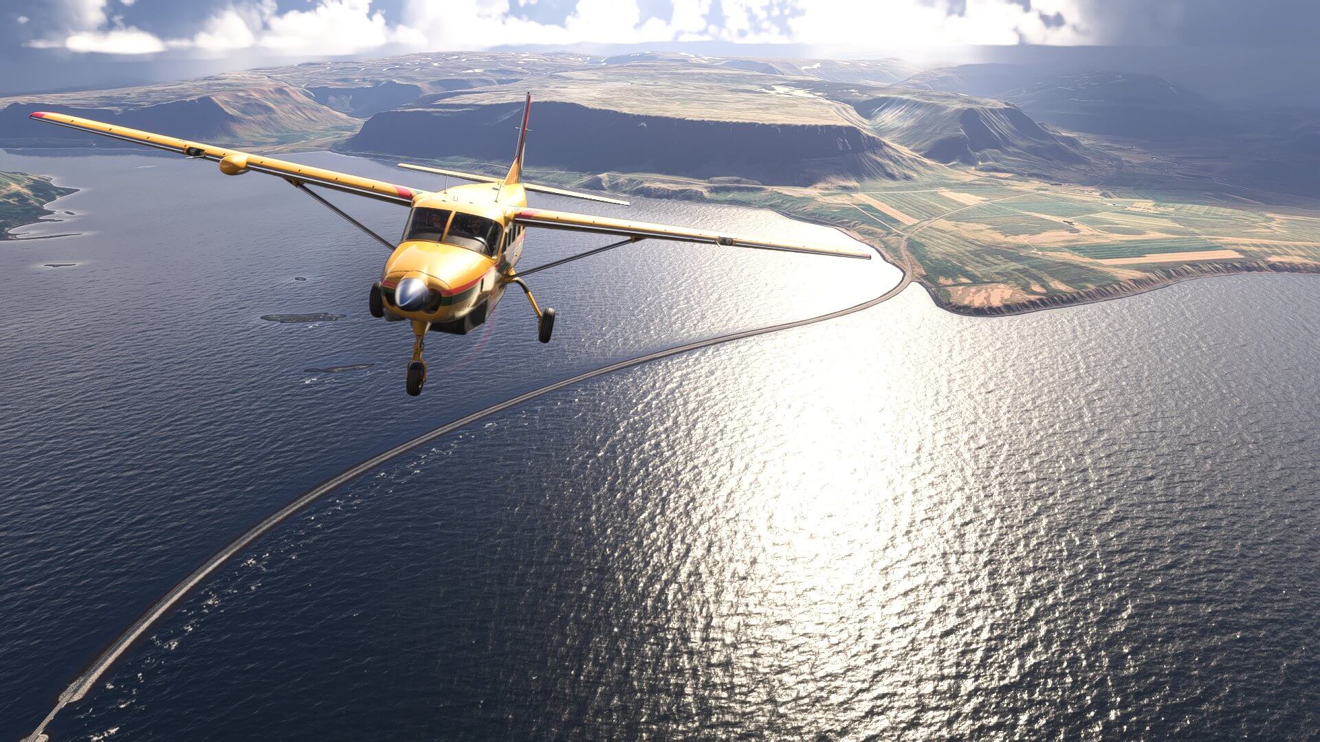 A high wing propeller aircraft flies over water with a bridge below