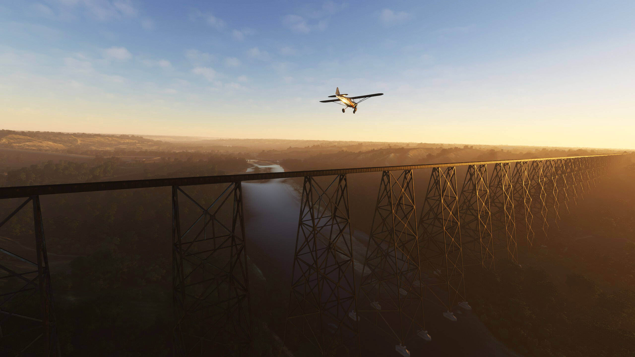 A high-wing propeller aircraft flies in parallel with a large bridge
