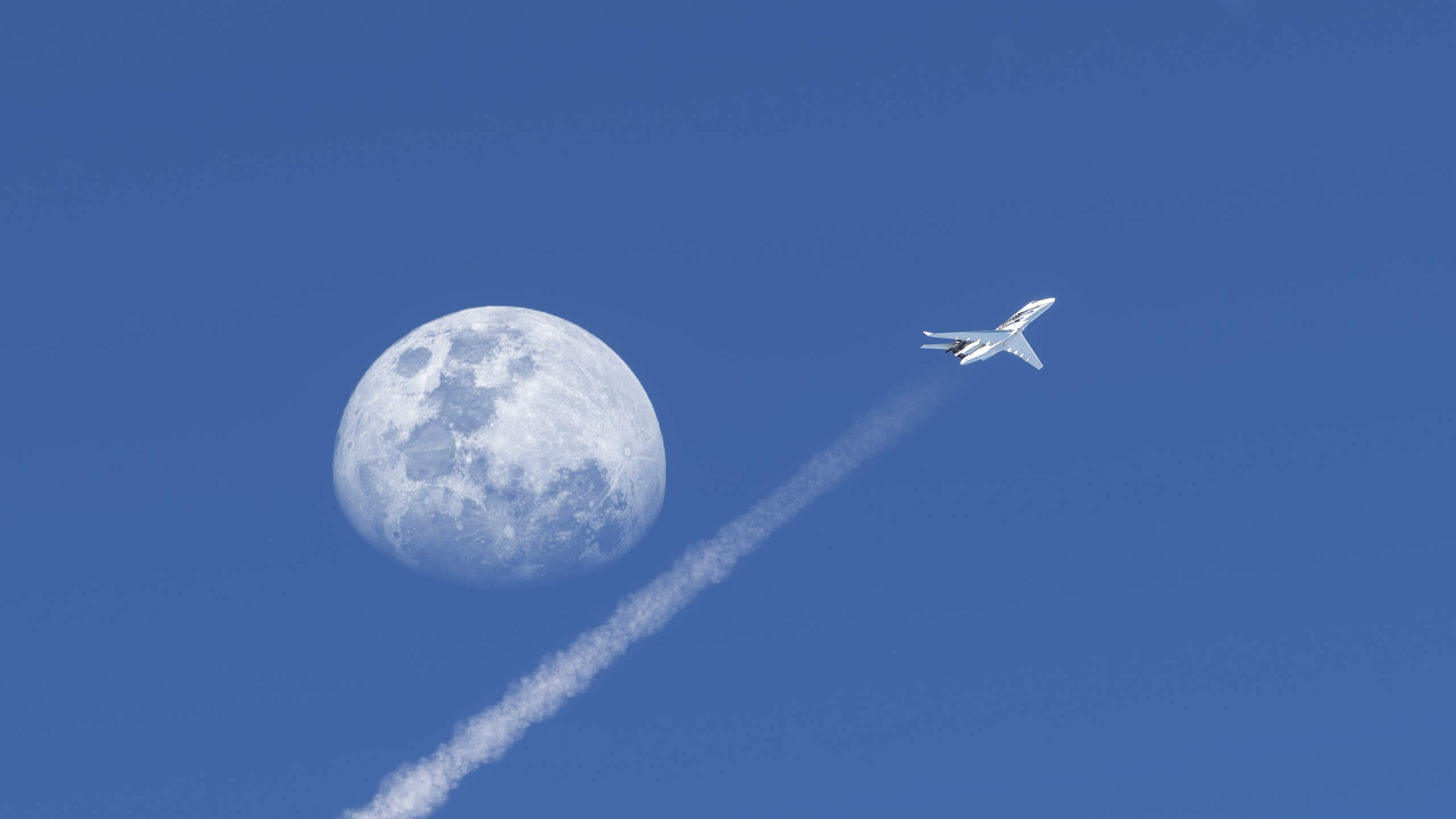 A business jet cruising at high altitude with the moon in view above