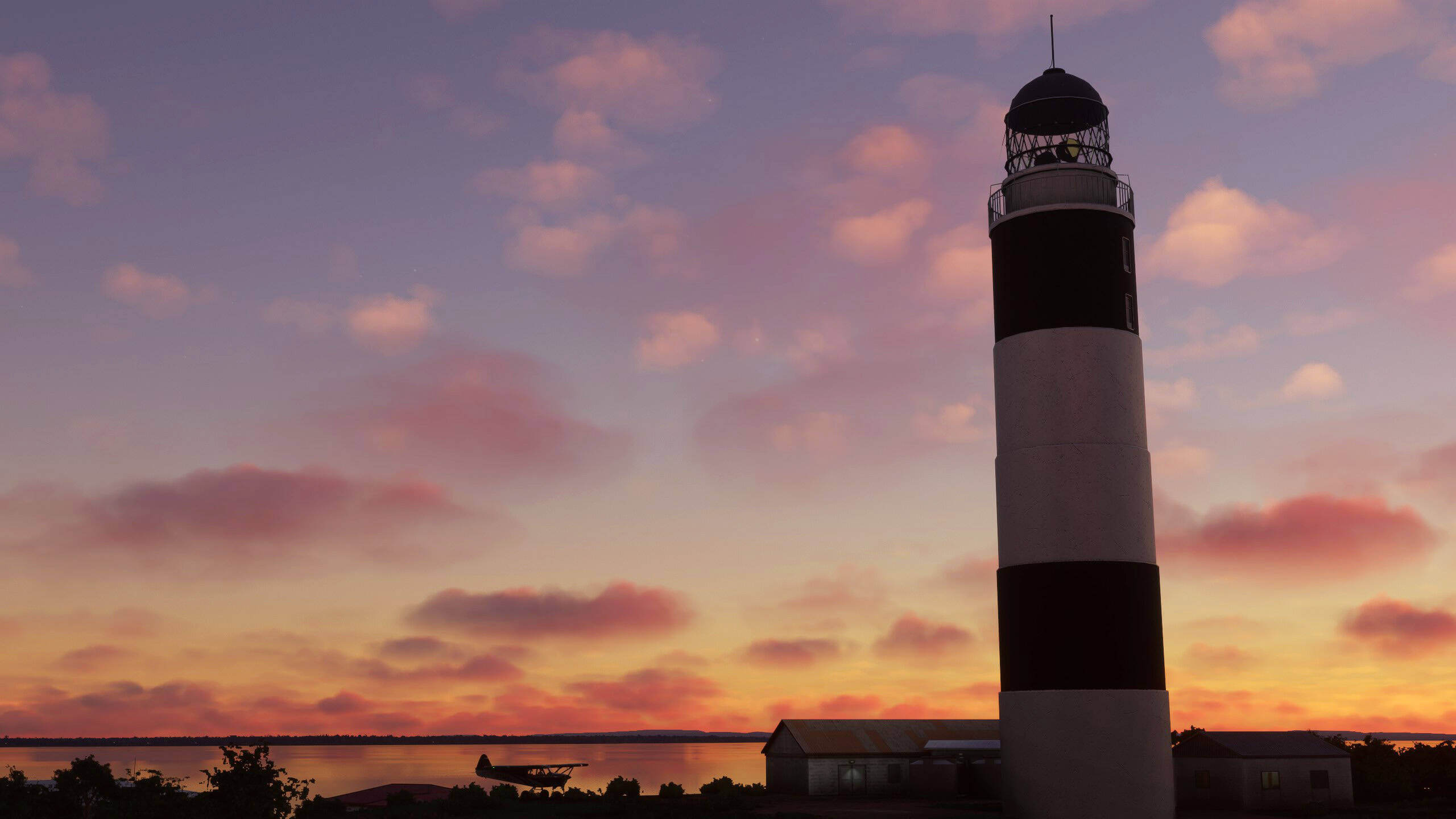An aircraft silhouetted on the ground next to a lighthouse after sunset