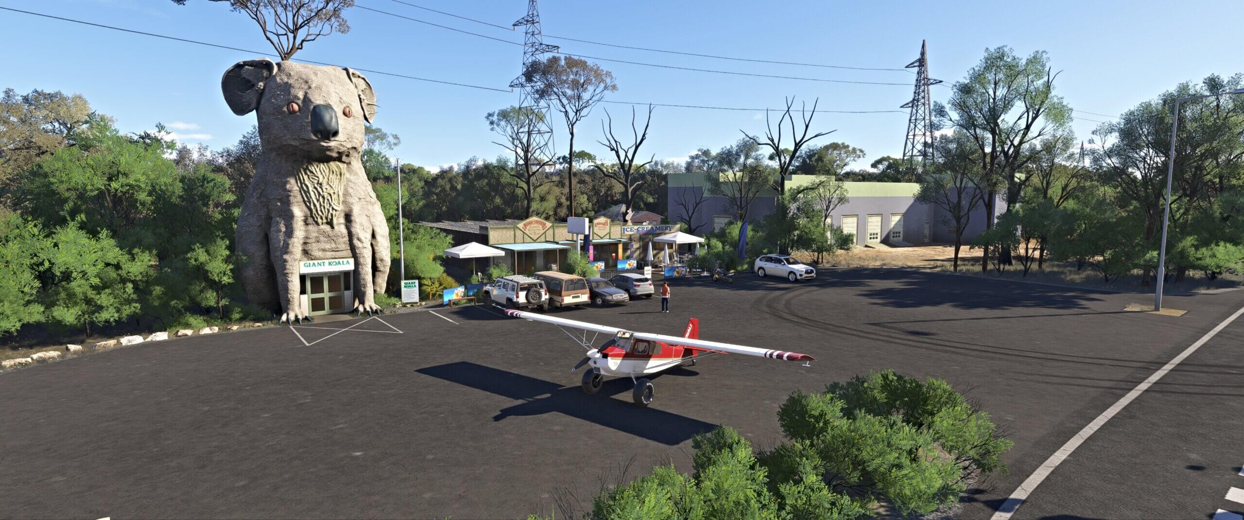 A high wing prop aircraft parked on the car park next to a giant Koala statue