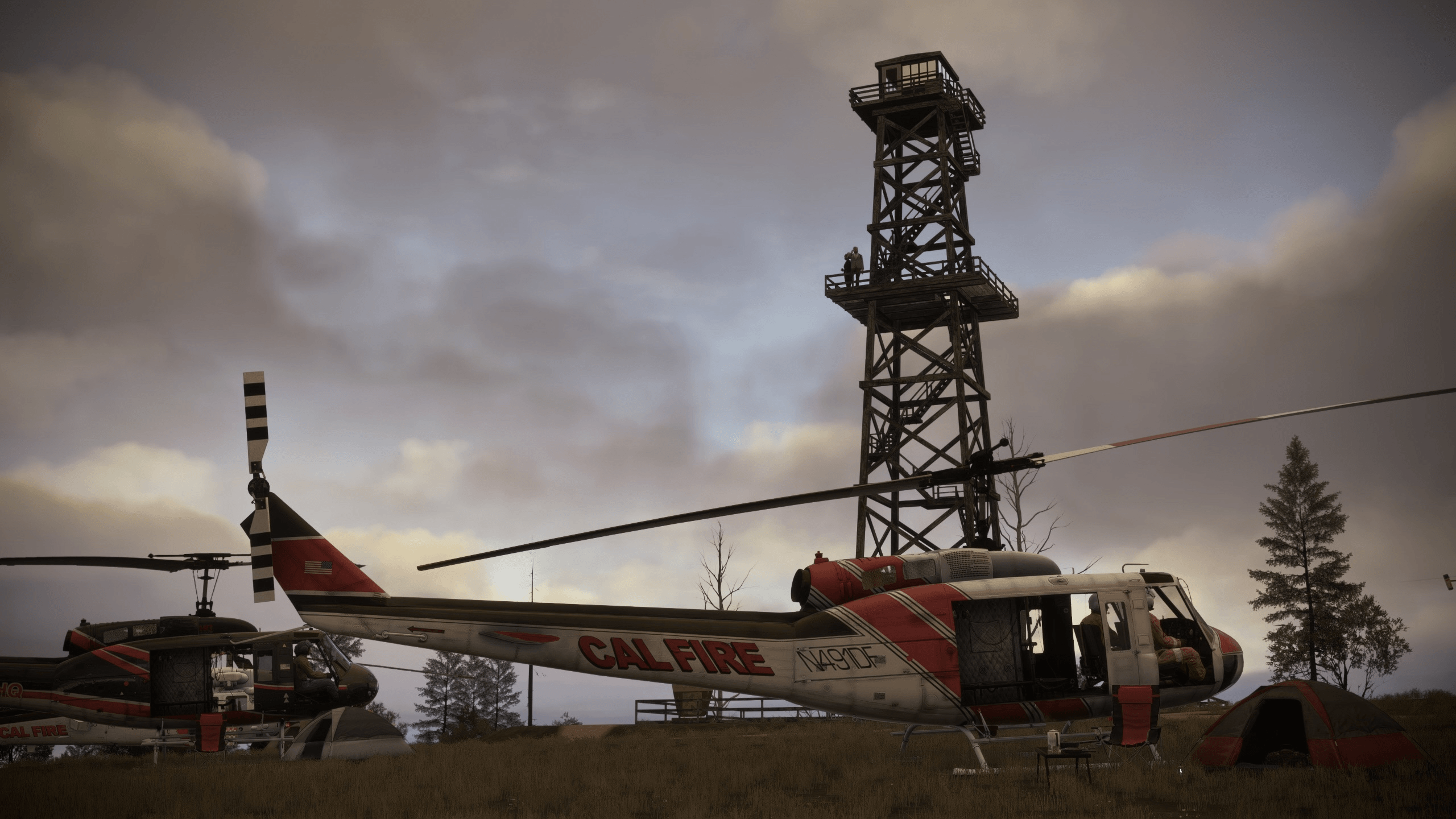 A number of firefighting helicopters parked on the ground near a fire watch tower