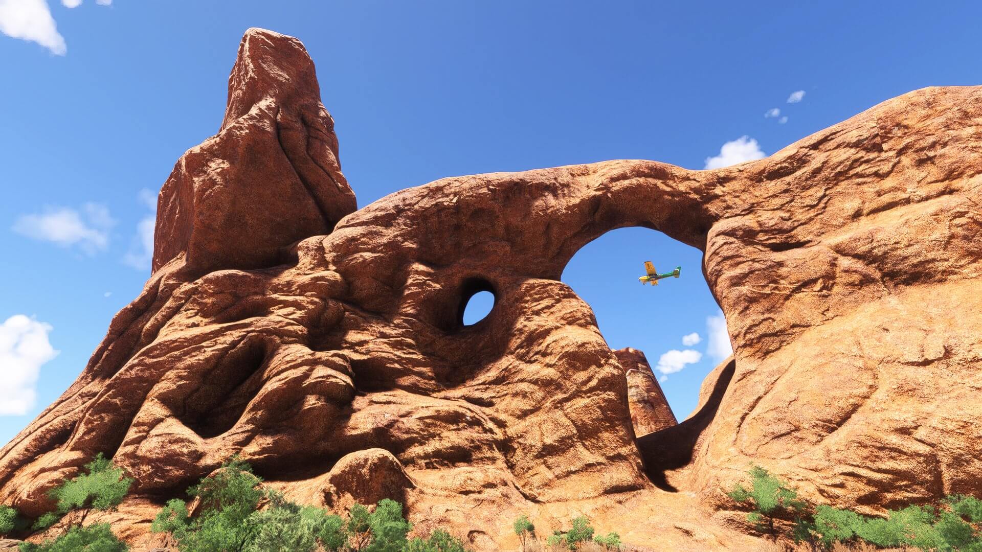 A high wing propeller aircraft flies through a desert landscape