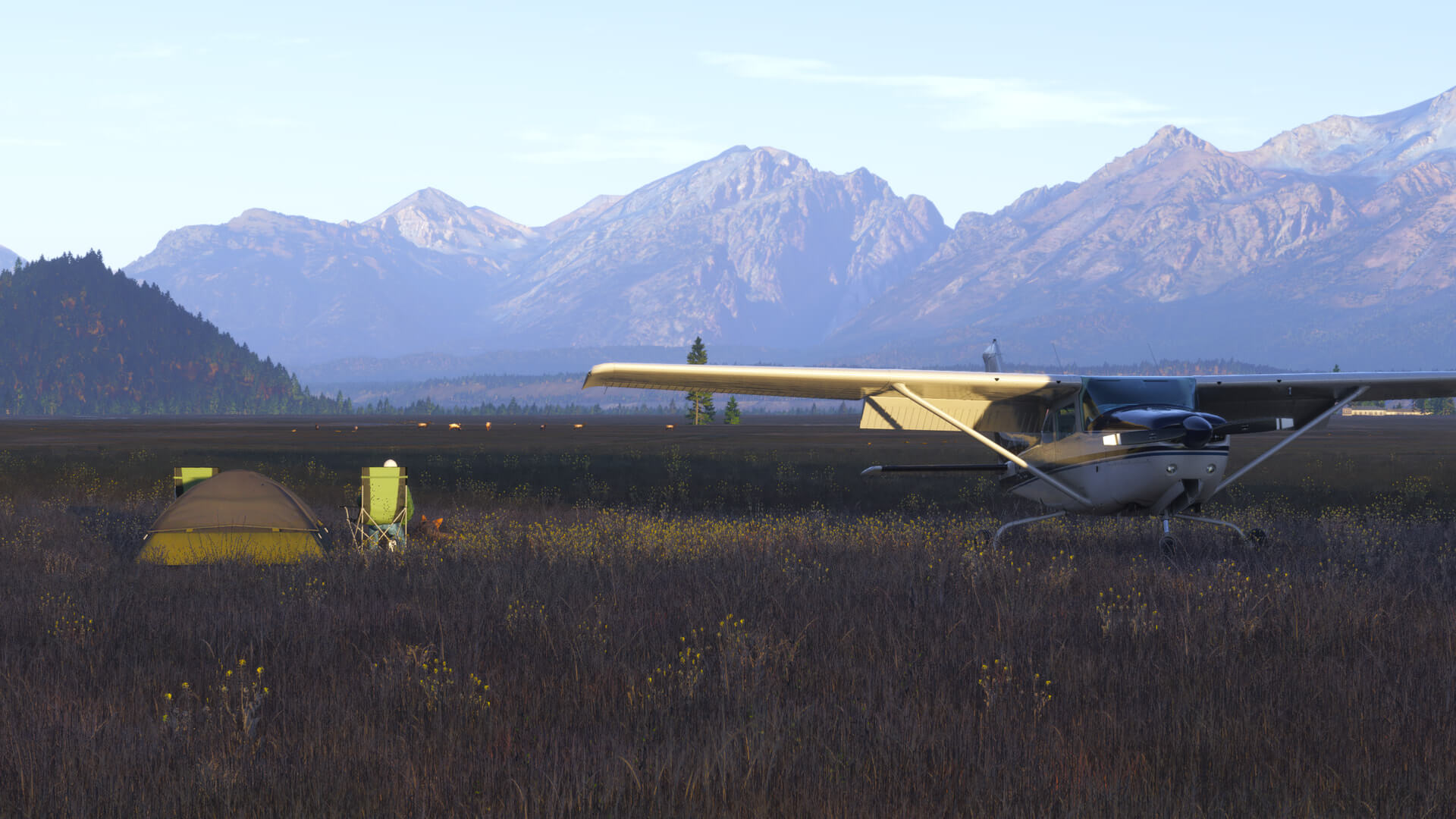 A Cessna sits idle in a valley with the pilot sat in a chair next to their tent