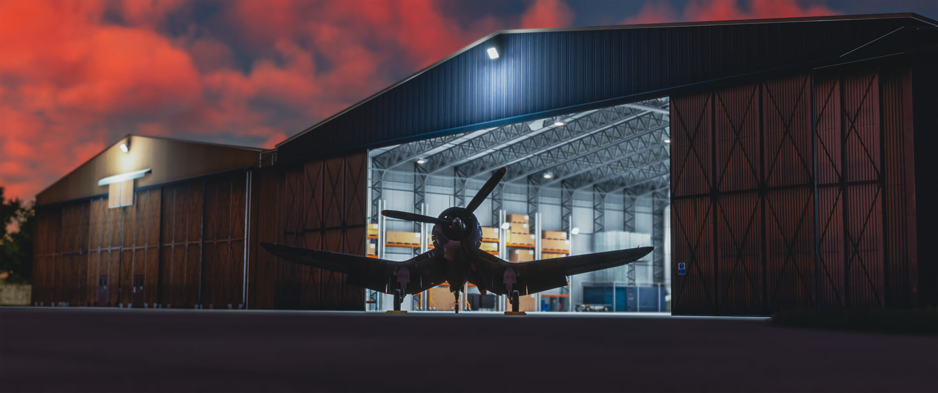 A Corsair jet sits idle on the ramp outside a hangar after sunset