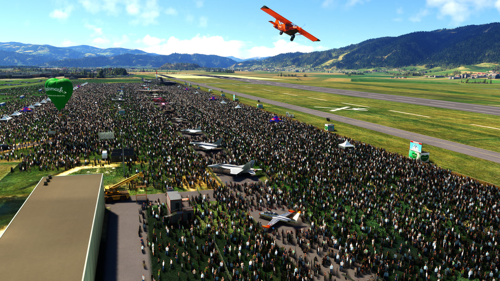 An orange high-wing propeller aircraft flies over a crowd at an airshow