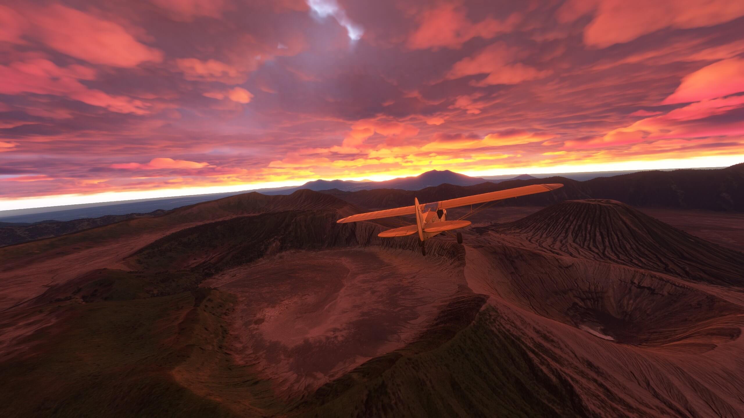 A yellow high wing aircraft flies over mountainous terrain after sunset