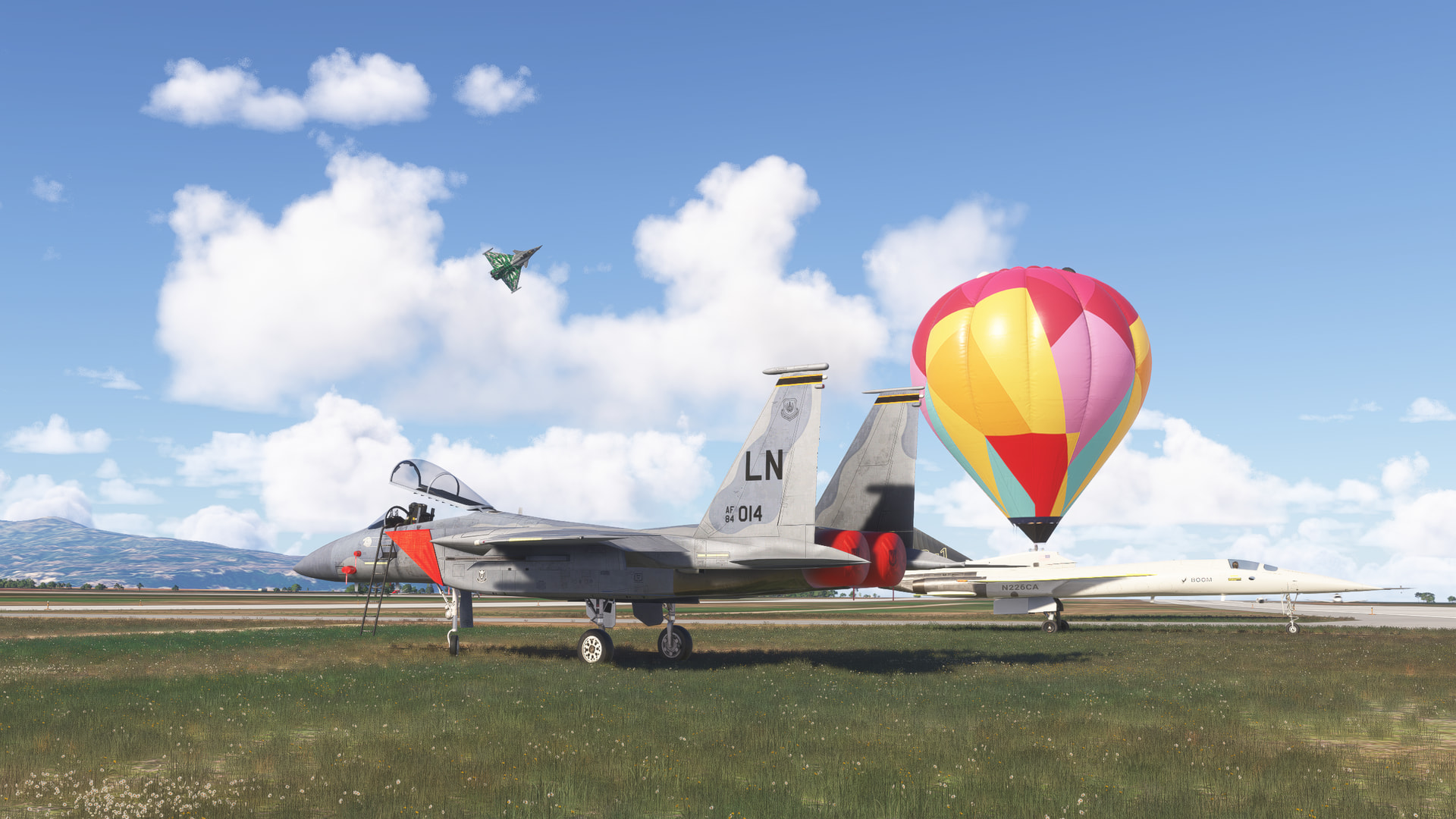 Fighter aircraft parked on grass with a hot air balloon next to them, and another fighter jet flying overhead